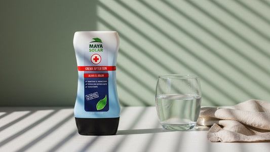 Crema After Sun de Maya Solar de 204 ml sobre una mesa clara, junto a un vaso de agua y un lienzo de lino arrugado, contra una pared verde salvia con la sombra rayada de una persiana