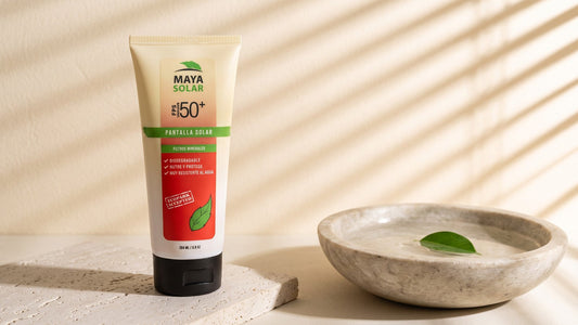 Bloqueador Solar Crema FPS 50+ Biodegradable de Maya Solar de 204 ml de pie sobre una losa de piedra caliza, junto a un cuenco de piedra con una hoja verde flotando en agua