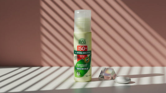 Bloqueador Solar Crema FPS 50+ Biodegradable de Maya Solar de 75 ml de pie sobre una superficie blanca, frente a una pared rosada con la luz rayada de una persiana, junto a un prisma de vidrio y una piedra blanca