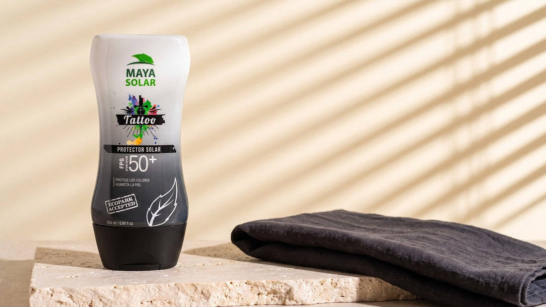 Bloqueador Solar para Tattoos FPS 50+ de Maya Solar de 204 ml de pie sobre una losa de piedra caliza, junto a una tela gris oscura doblada, con la luz de una persiana rayando la pared