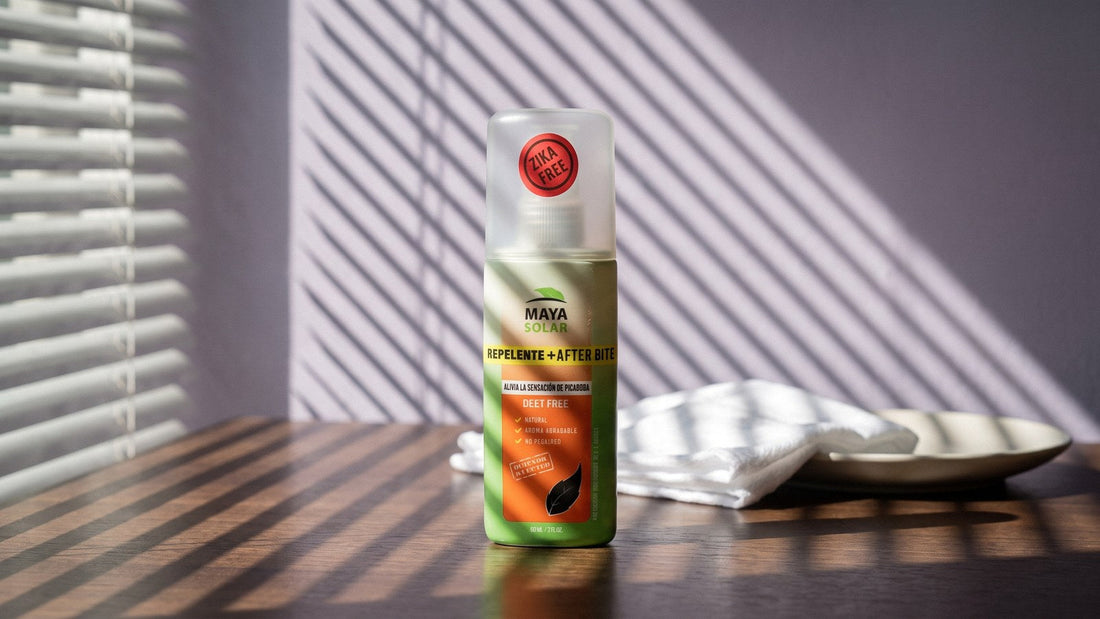 Repelente de mosquitos con AfterBite de Maya Solar en spray de 60 ml sobre una mesa de madera oscura, junto a un paño de algodón blanco y un plato de cerámica, con la luz rayada de una persiana en la pared